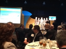 Photo of individuals eating dinner at tables and watching announcements on stage at the Governor’s ImPAct Awards