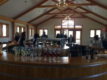 View from behind the bar of individuals socializing, dozens of wine glasses are stacked on the bar top in the foreground