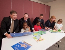 Group of adults and children at Pocono Services for Families & Children’s Book Ownership Program seated behind a table with children's books in front of them