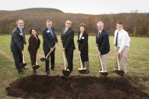 Individuals in suits pose with shovels in hand on a field for the ground breaking of the New Monroe Campus