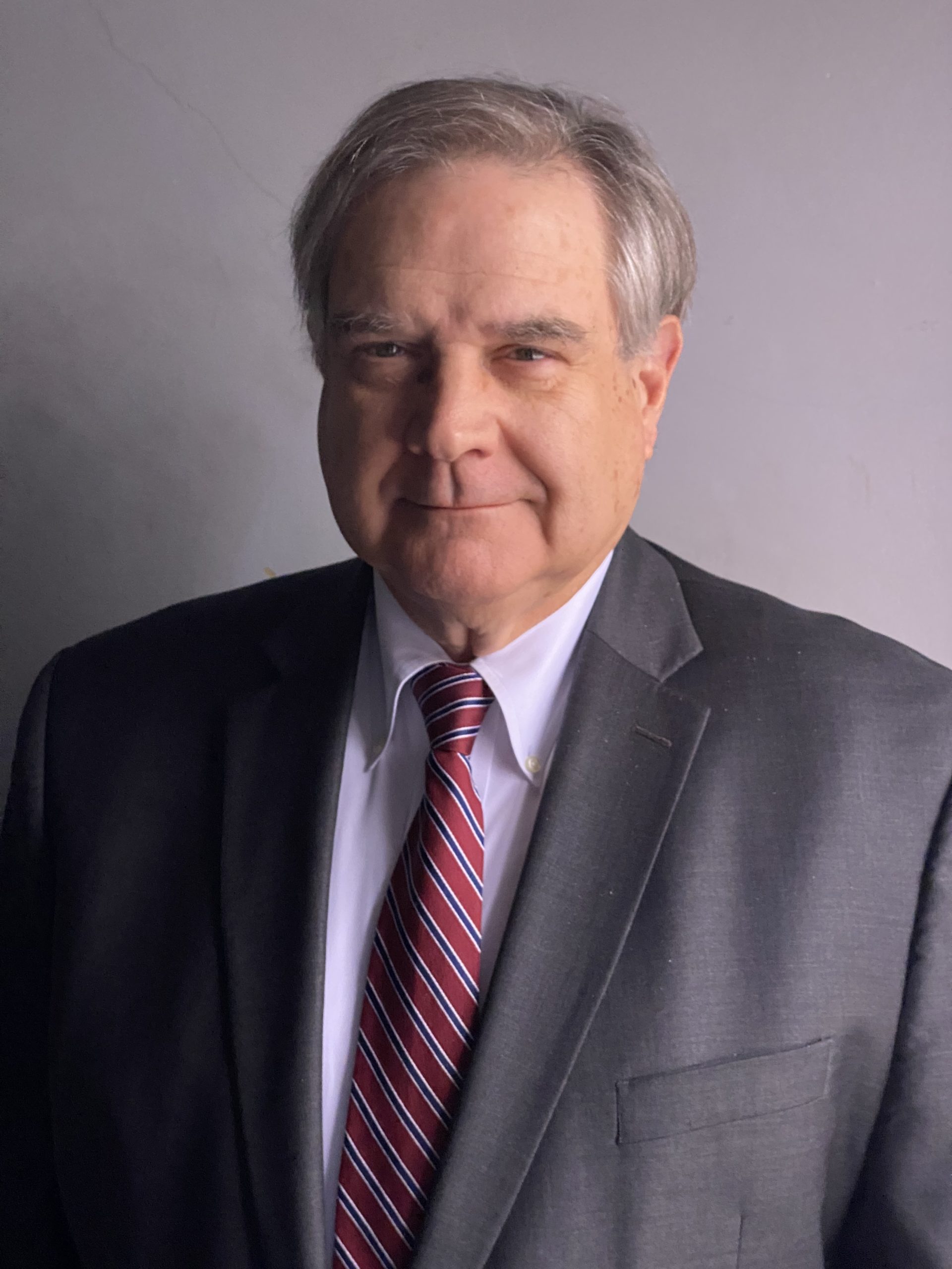 Portrait head shot of Charles Leonard, a man with dark short hair, wearing a white collared shirt with a black blazer and dark patterned tie