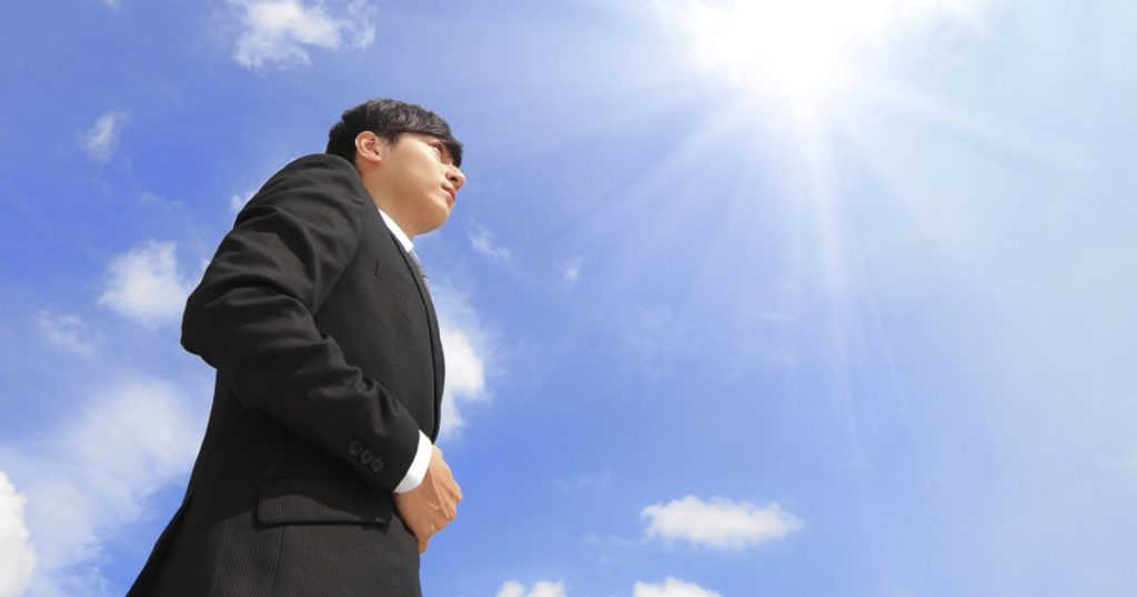 Successful business man standing over blue sky and purposefully looking away